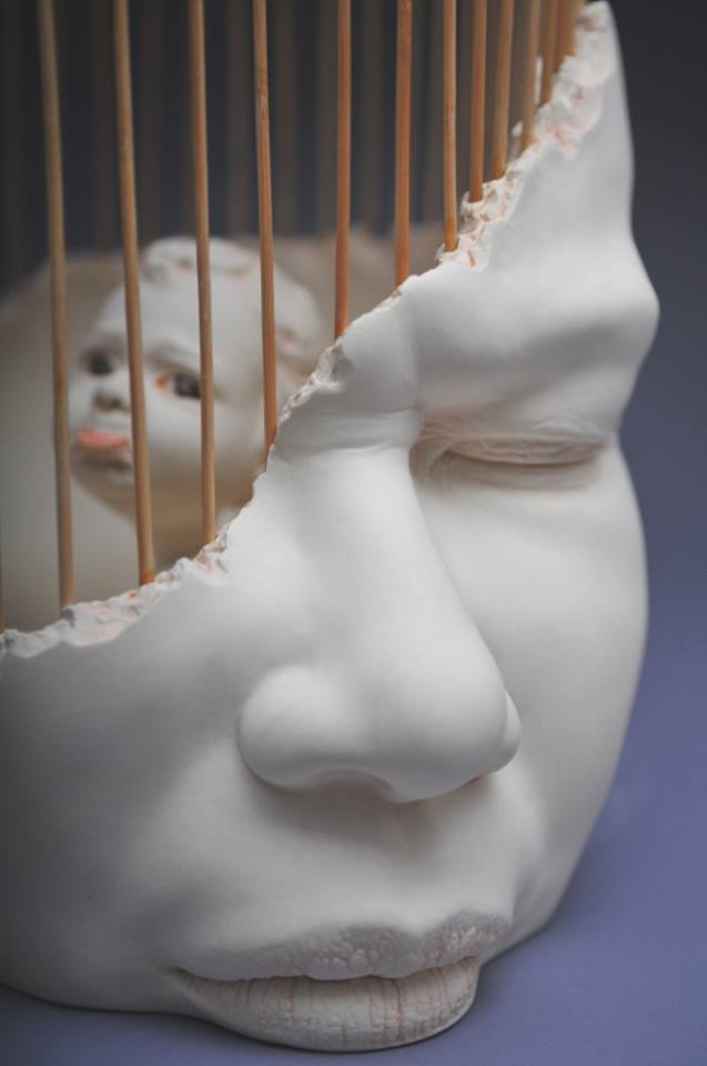 Un visage sculpté blanc et au travers une grille et un petit visage d'enfant